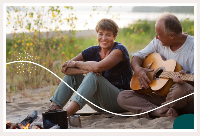 Happy Elderly Couple Sitting Around Campfire, Husband Playing Guitar
